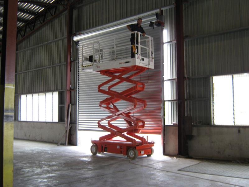 A United Doors technician on a scissor lift installing an industrial roller door